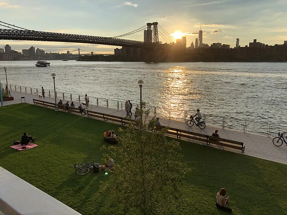 Domino Park's lawn and riverside path at sunset, the Williamsburg Bridge beyond