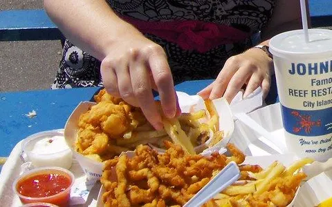 Fried clams and fries on a picnic table beside a Johnny's Reef cup